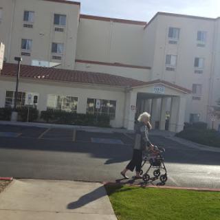 A senior person walking with a walker in front of a hotel on a sunny day.