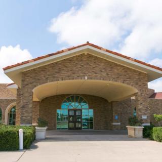 A building entrance with a stone facade and arched design under a partly cloudy sky.