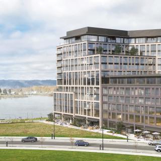 A modern apartment building overlooking a waterfront, with a view of distant hills and open sky.