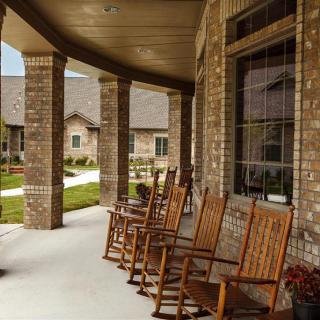 A row of wooden rocking chairs on a brick porch in a residential neighborhood.