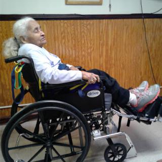 An elderly person comfortably seated in a wheelchair, inside a cozy environment.