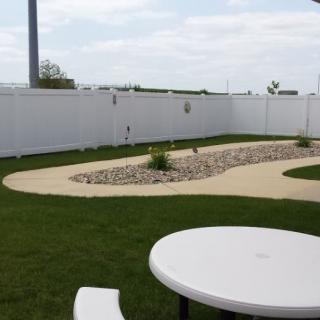 A neatly landscaped backyard featuring a white fence, grassy lawn, and a curved pathway.