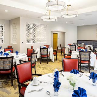 A well-appointed dining room with elegantly set tables featuring blue napkins and comfortable red chairs.