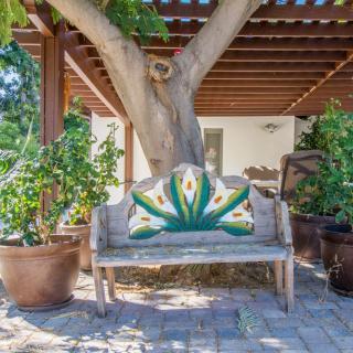 A rustic wooden bench with colorful decorative backrest under a tree on a patio.