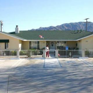 A charming residential house with a fenced front yard set against a mountainous backdrop on a sunny day.