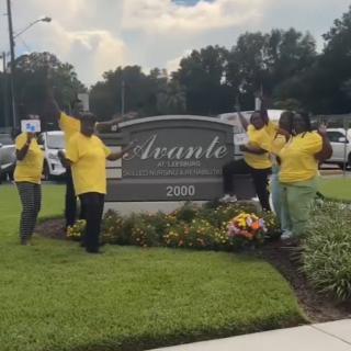 A joyful group in yellow shirts celebrating by a community sign.