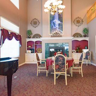 A luxurious living room with a high ceiling, featuring a fireplace, dining table, chairs, and a piano.