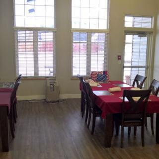 A well-lit dining area with tables covered in red tablecloths, surrounded by chairs and large windows.