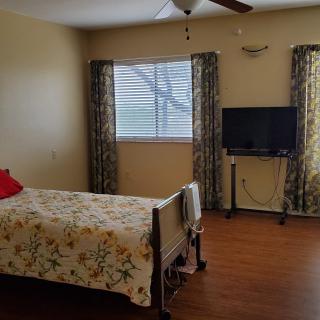 A cozy bedroom with a floral-patterned bed, window draped with curtains, and a TV on a stand.