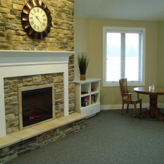A cozy living room featuring a stone fireplace with a clock above it, alongside a small table and chairs near a window.