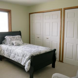 A simple bedroom featuring a single bed, closet doors, and a window.
