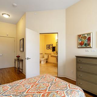 A cozy bedroom with a patterned bedspread, a dresser, and an open doorway leading to a bathroom.
