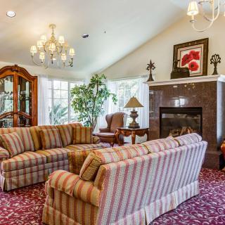 A cozy living room featuring striped sofas, a chandelier, and a fireplace with artwork above it.