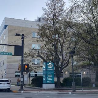 A view of an urban building with a prominent sign, surrounded by trees and street elements.