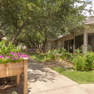 A peaceful garden with a pathway leading to a house, surrounded by trees and vibrant flowers.