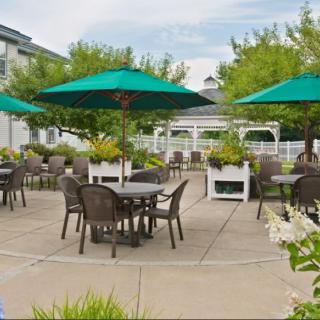 A spacious outdoor patio with tables, chairs, and green umbrellas surrounded by greenery and a gazebo in the background.