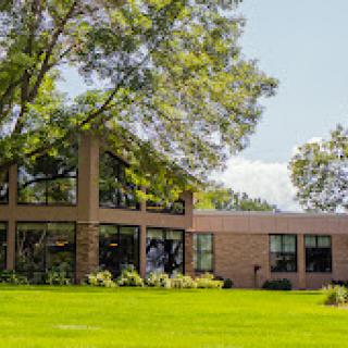 A modern building surrounded by lush green grass and trees under a clear blue sky.