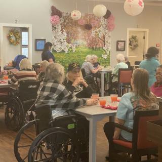 A group of elderly individuals in a nursing home, some in wheelchairs, enjoying a social activity together.