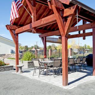 An outdoor pergola with a seating area, featuring a table, chairs, and an American flag.