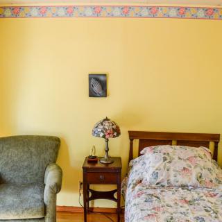 A cozy bedroom with a floral bedspread, vintage lamp, and comfortable chair.