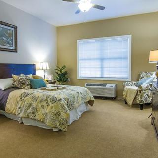 A cozy and well-decorated bedroom with a bed, bedside table, lamps, and a window.