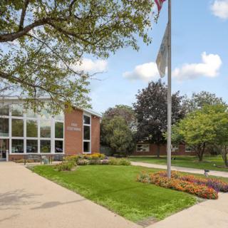 A school building with a flagpole and landscaped surroundings on a cloudy day.