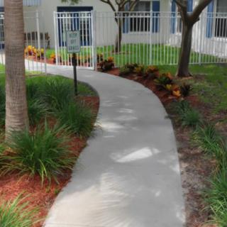 A curved pathway through a landscaped garden with trees and plants, bordered by a white fence.