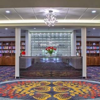 A modern lobby with a reception desk, surrounded by bookshelves and decorated with a colorful carpet.