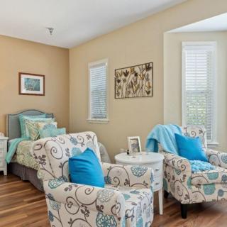 A cozy bedroom with stylish decor, featuring a bed with blue accents, patterned chairs, and framed artwork on the walls.