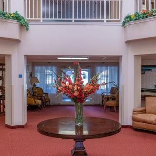 A spacious lobby with a central flower arrangement on a wooden table, surrounded by comfortable seating.