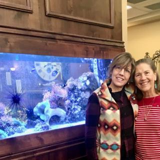 Two friends enjoying a moment in front of a vibrant aquarium.