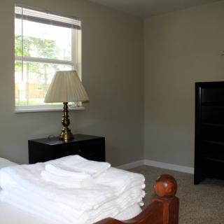 A minimalist bedroom with a window, lamp, and neatly folded linens on the bed.