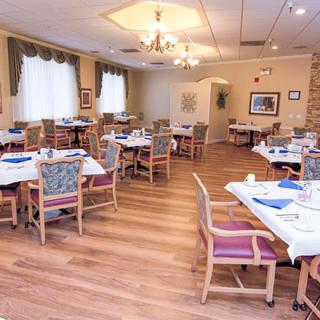 An empty dining room with neatly arranged tables and chairs, featuring wood flooring and soft lighting.