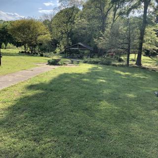 A serene garden landscape with a grassy area, trees, and a pathway on a sunny day.