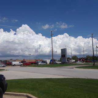A sunny day with fluffy clouds over a parking lot filled with vehicles.