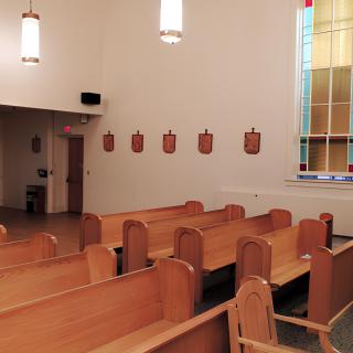 Interior of a church with wooden pews and a stained glass window.