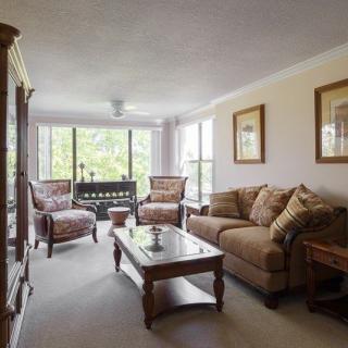A cozy living room with a sofa, armchairs, and a coffee table, illuminated by natural light from large windows.