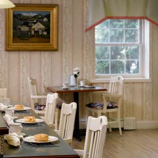 A cozy dining area with neatly arranged tables and chairs, featuring a window and wall art.
