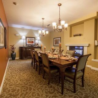 A warmly lit dining room with a large table set for dinner, featuring elegant chairs and chandeliers.