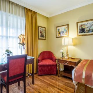 A cozy hotel room with classic decor, featuring a bed, desk, and seating area.