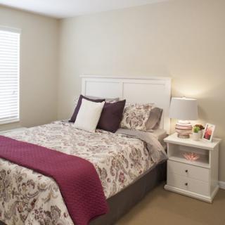 A cozy bedroom with a well-made bed and a nightstand with a lamp.