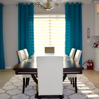 A modern dining room with a dark wooden table, white chairs, and turquoise curtains.