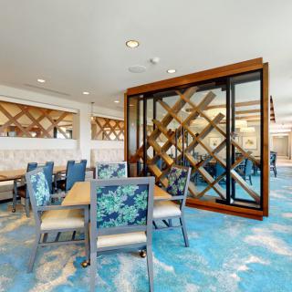A modern restaurant interior with blue carpeting, wood accents, and tables and chairs arranged for dining.