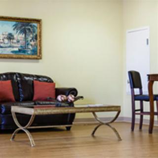 A cozy living room with a black sofa, red pillows, and a glass coffee table set against a painting and wooden floor.