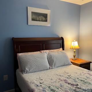 A cozy bedroom featuring a neatly made bed, a nightstand with a lamp, and tasteful artwork on the wall.
