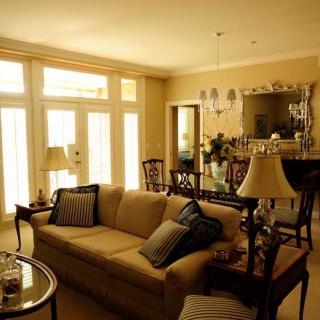 A warmly lit living room featuring elegant furniture, including a sofa and chairs, with natural light streaming through large windows.