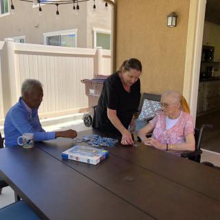 Three people enjoying a conversation over a puzzle at an outdoor table.