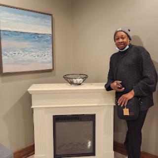 A person stands beside a stylish fireplace, showcasing a serene painting of the ocean.