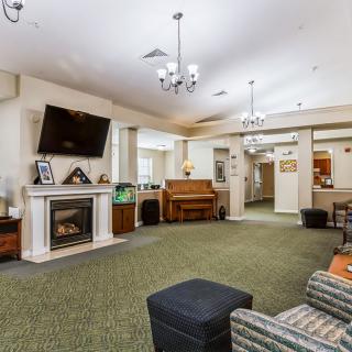 A cozy living room with a fireplace, television, and piano, adorned with elegant chandeliers and comfortable seating.