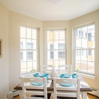 A brightly lit dining area with a neatly set table in front of large windows.